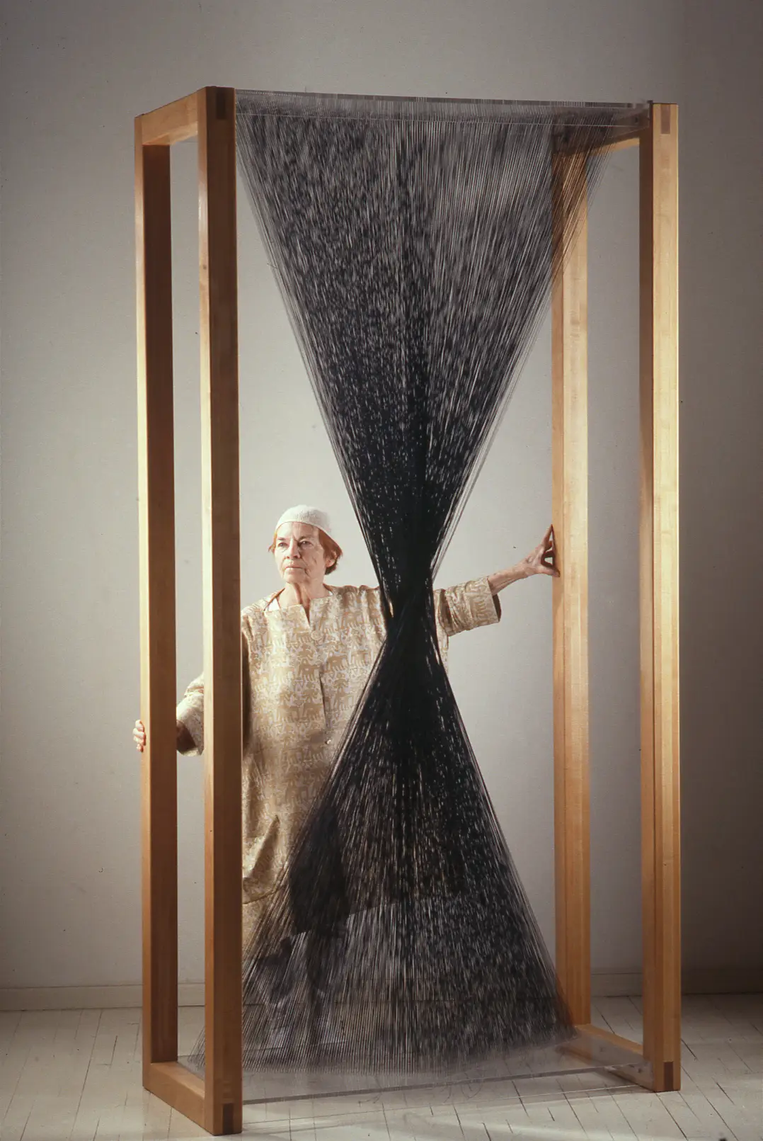 Lenore Tawney standing next to a large weave installation